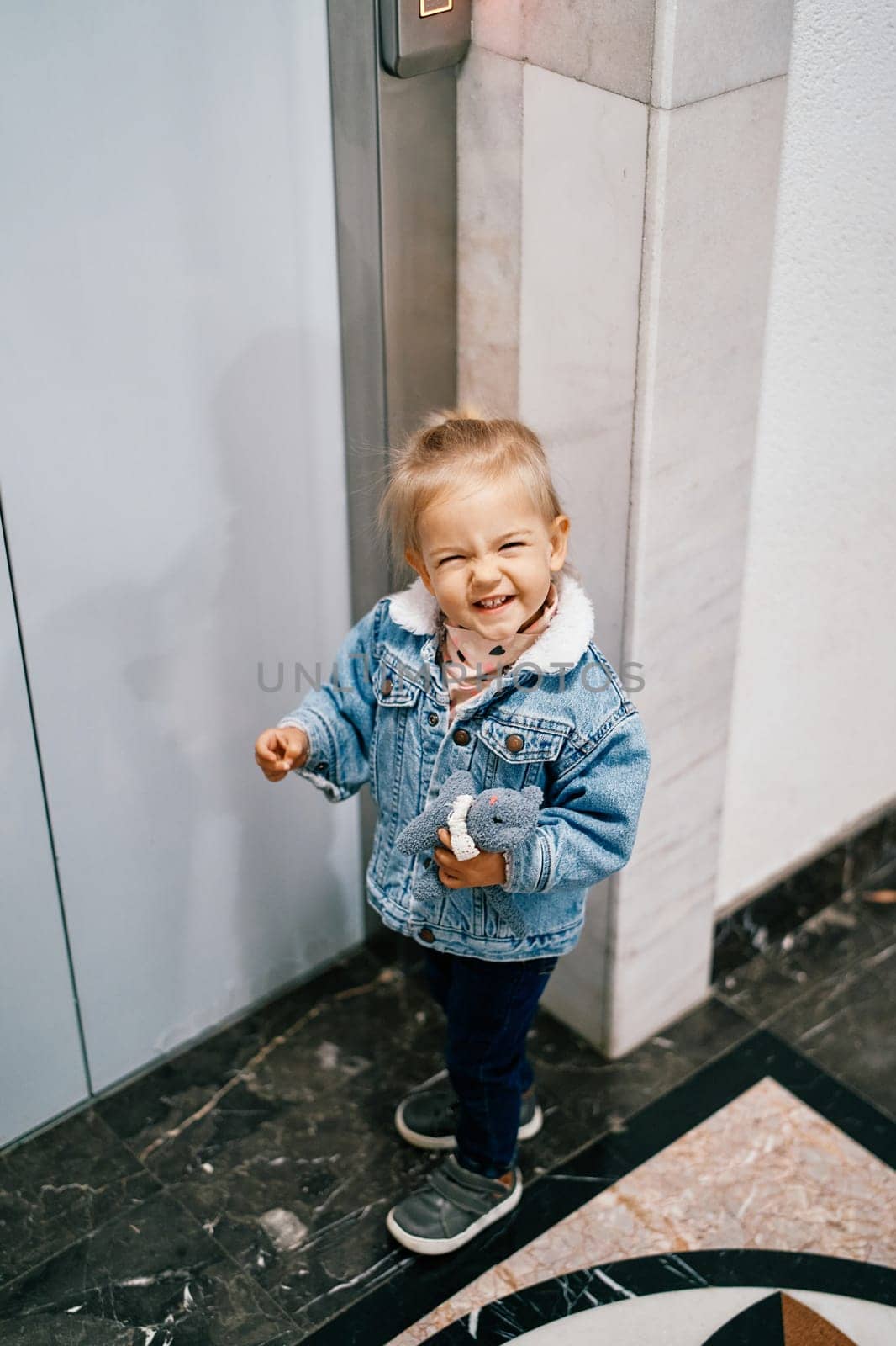 Little laughing girl stands with a toy in her hand near the elevator door. High quality photo