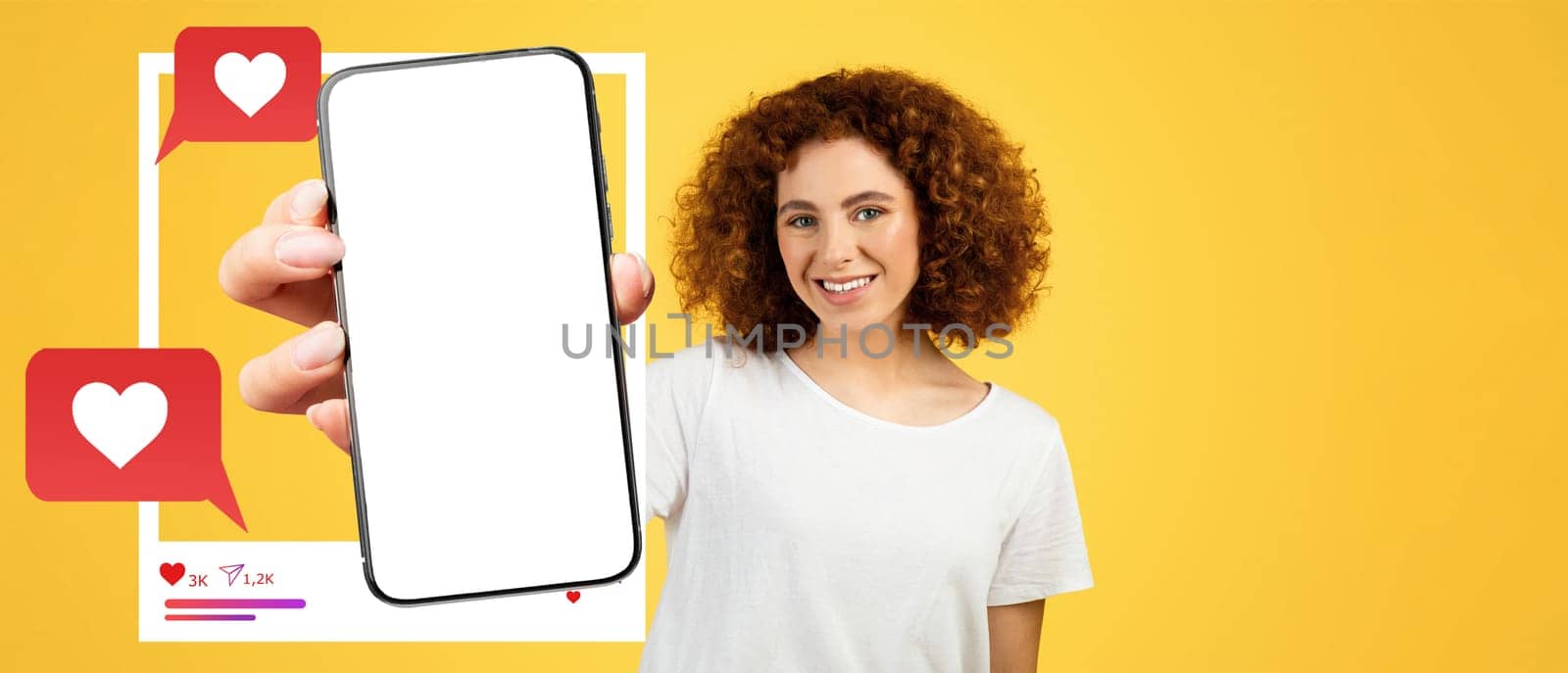 A cheerful influencer with curly hair holds a smartphone against a bright yellow background. The screen is blank, perfect for showcasing social media interactions like likes and messages.