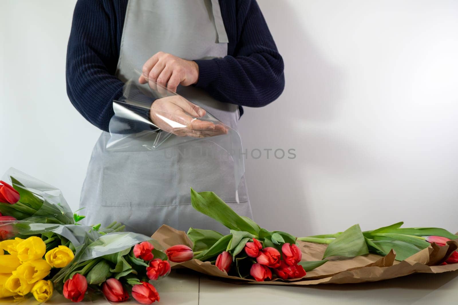 Caucasian male florist arranging tulip bouquets in apron.