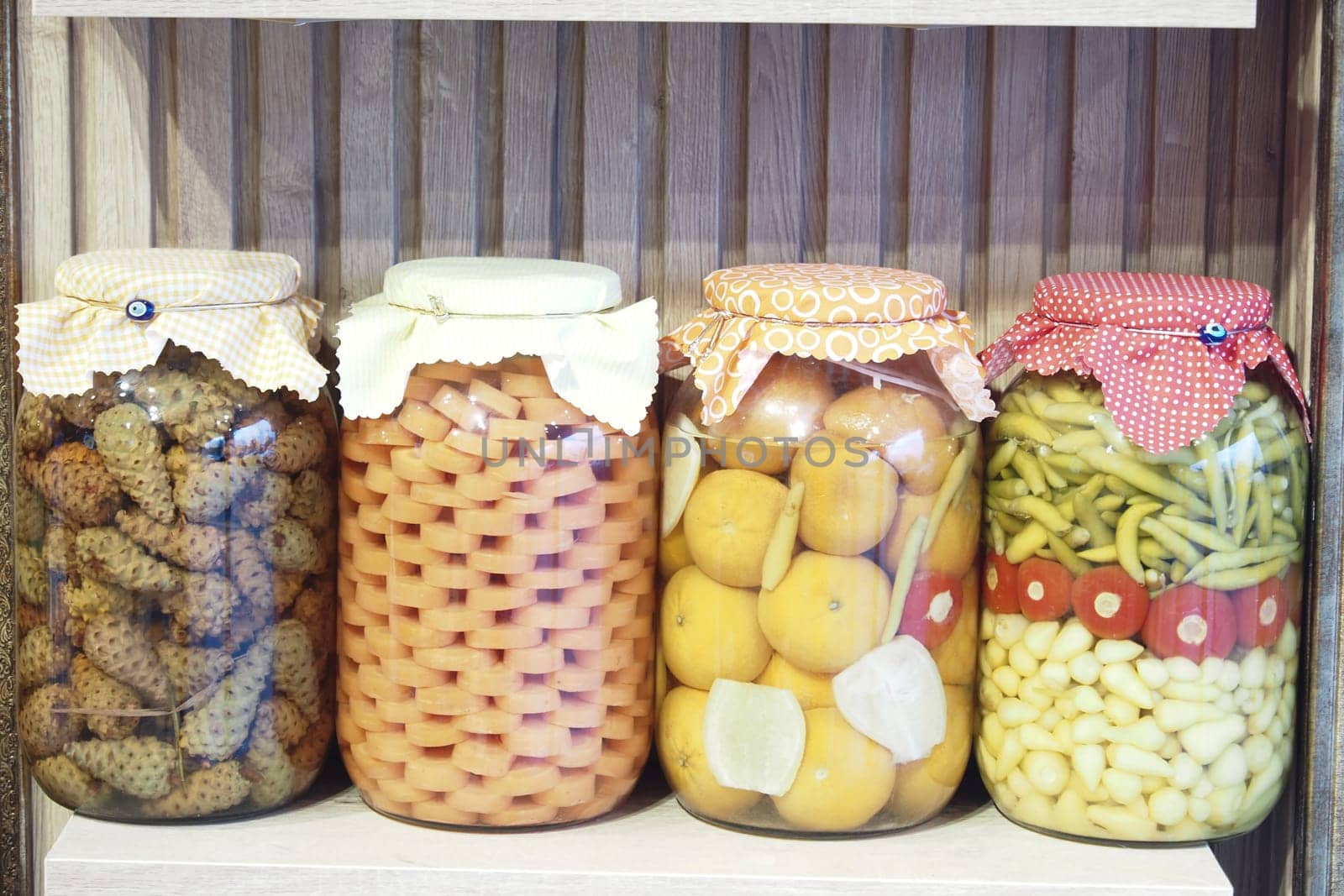 Preserved fruits and vegetables are neatly arranged on a wooden shelf.