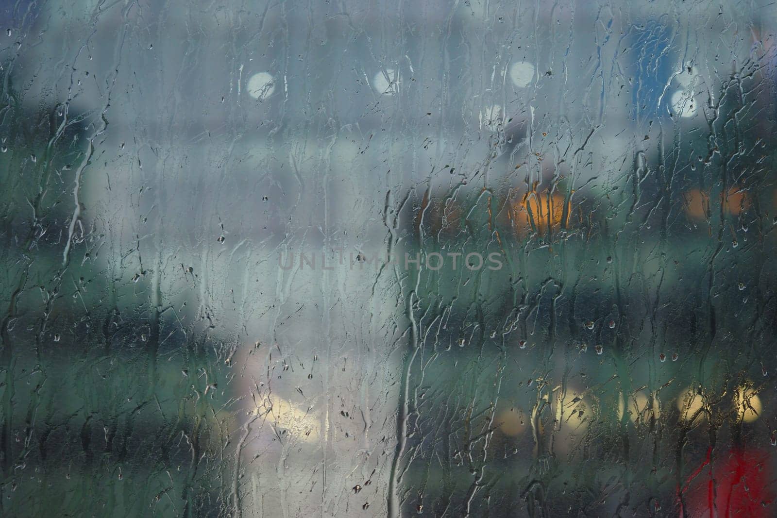 Raindrops trickle down a window, obscuring the cityscape behind.