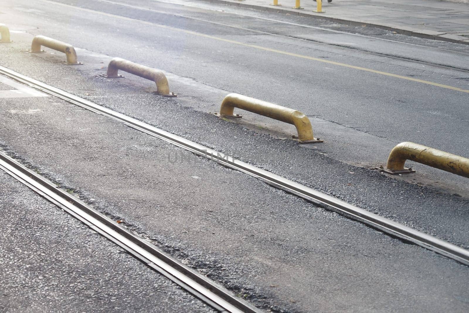 Metal tracks run parallel to yellow barriers on a calm city road.