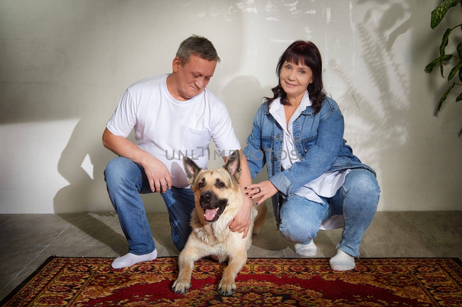 Middle-aged couple poses with their friendly German shepherd in their charming apartment, capturing a moment of love and togetherness.