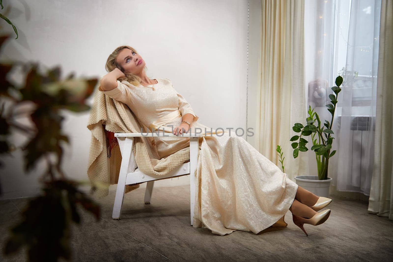 A middle-aged woman with blonde hair is relaxing and posing in a cozy indoor setting during a lifestyle photo shoot.