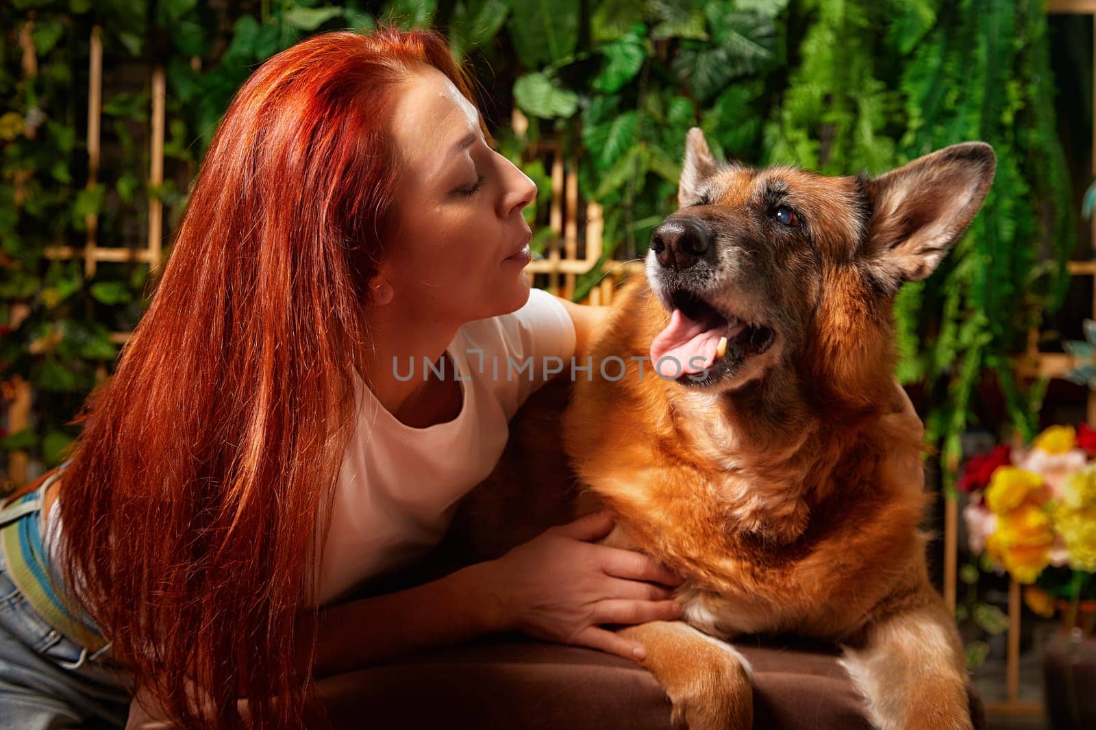A woman lovingly engages with her German Shepherd in a warm, inviting indoor space filled with plants.