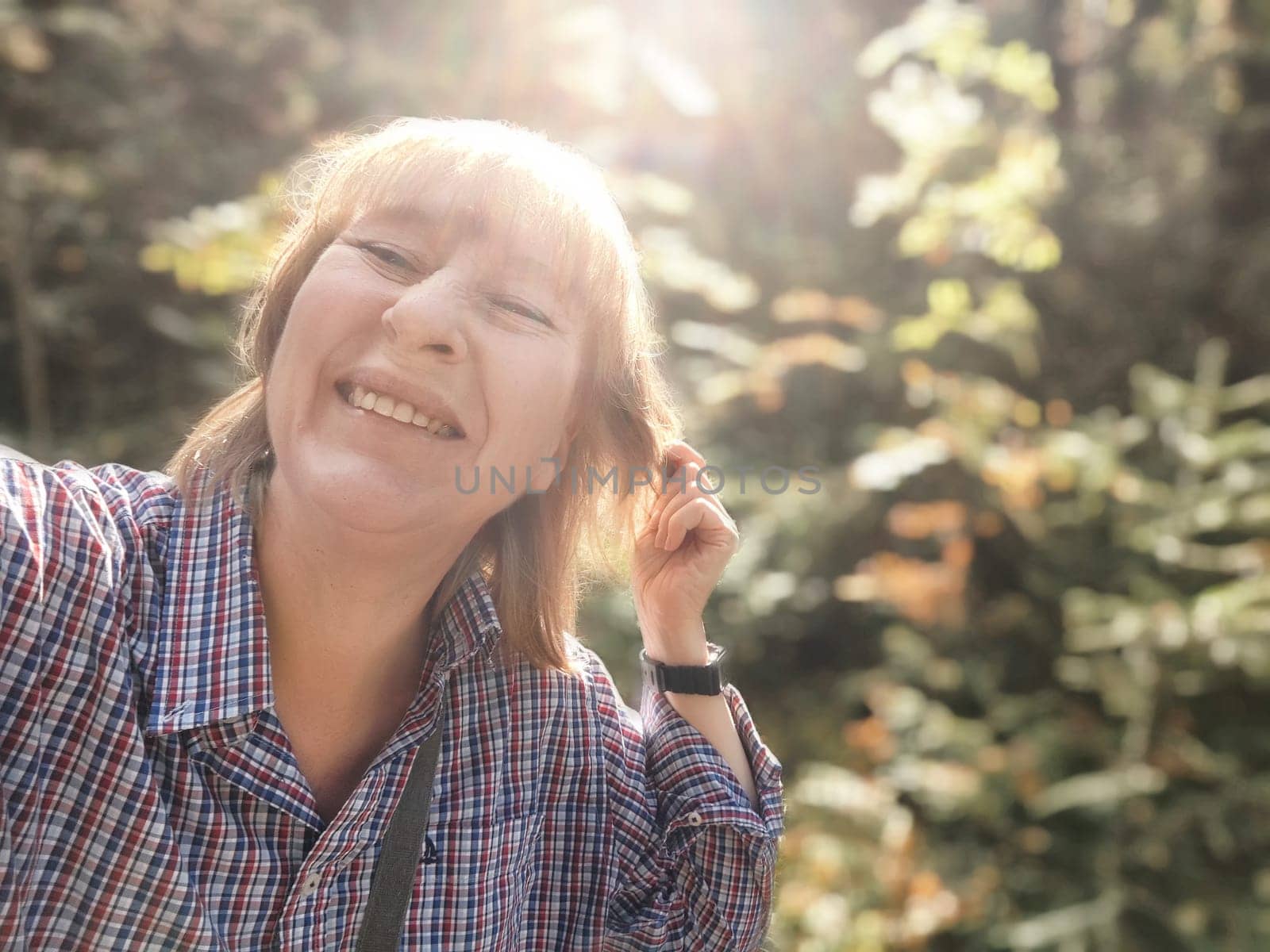 Blonde woman smiles brightly during her autumn adventure in a beautiful forest, capturing the moment in a joyful selfie.