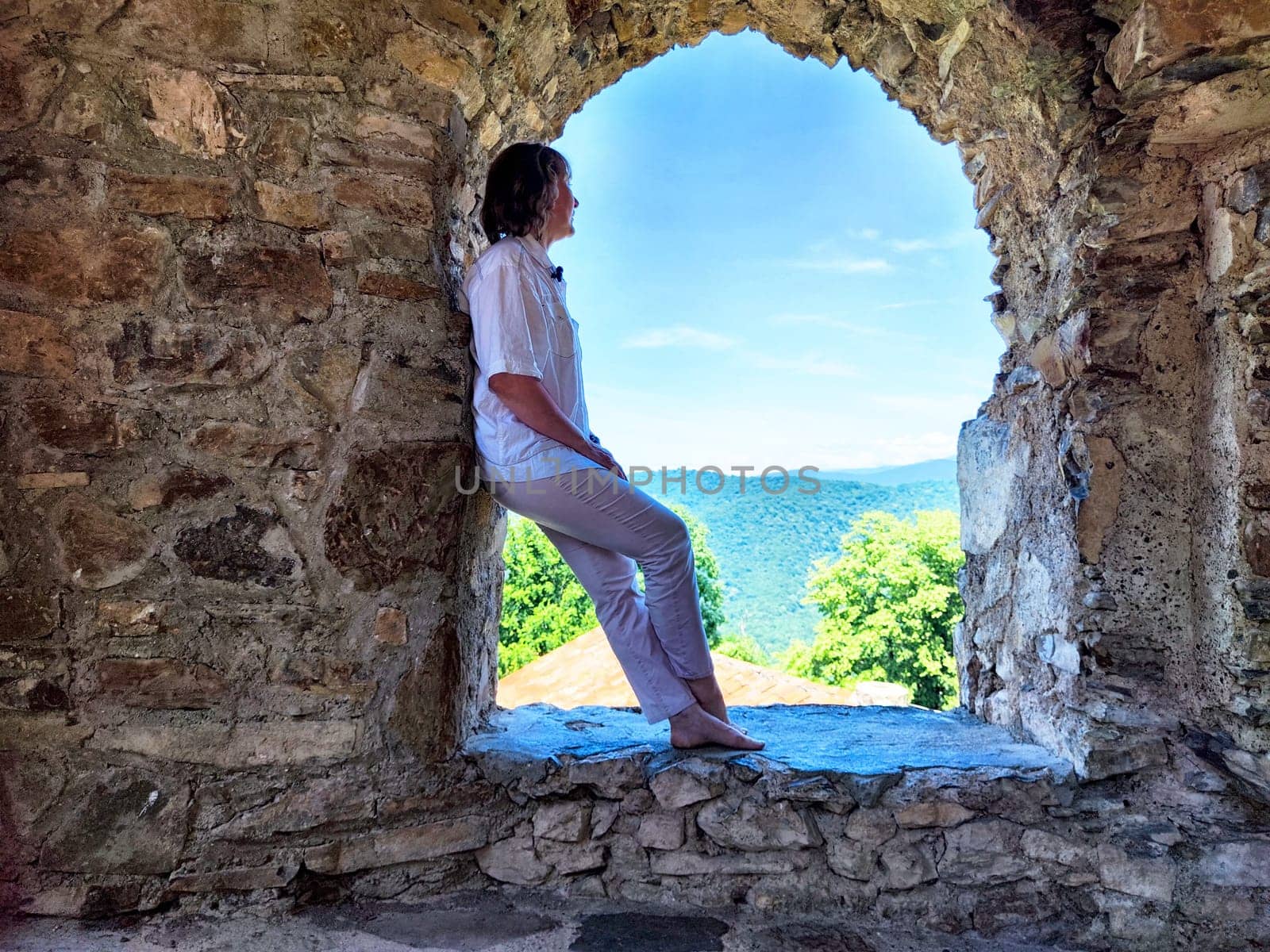 A woman enjoys a scenic view from a weathered stone archway while relaxing on a sunny afternoon.