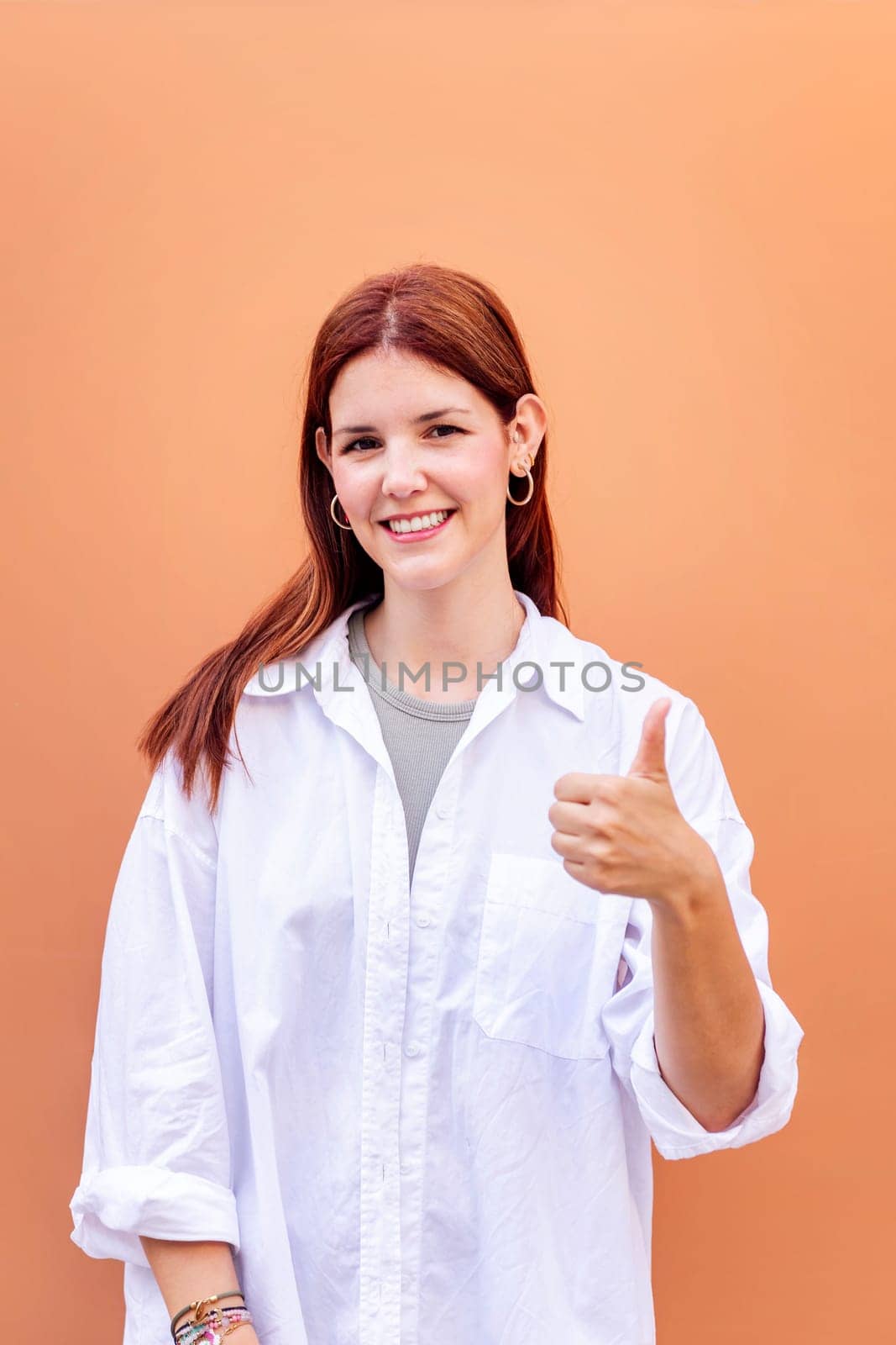 young woman giving a thumb up gesture while smiling looking at camera in a positive and friendly mood suggesting that she is happy and content, copyspace for text