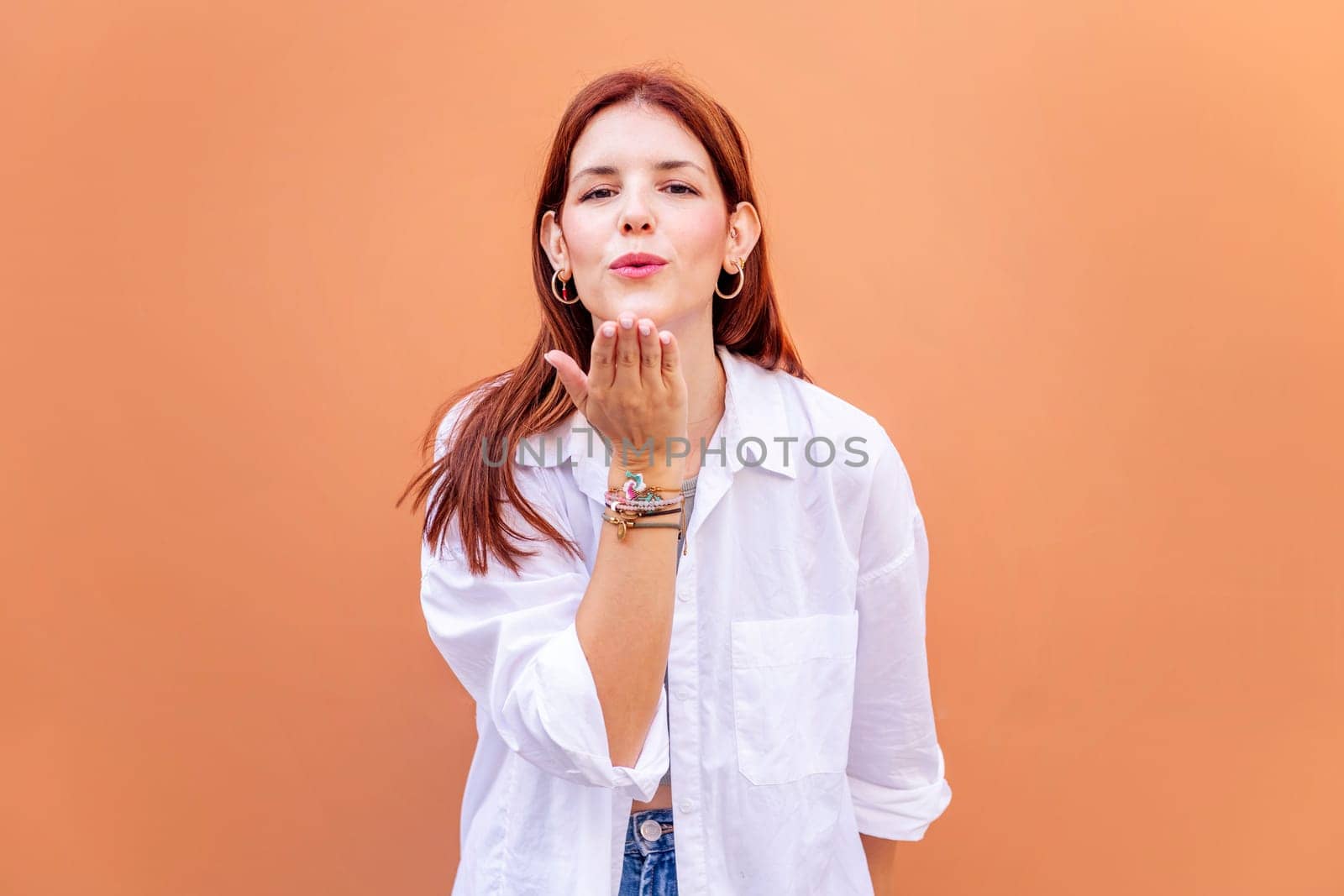 young woman giving a kiss with hand while smiling looking at camera in a positive and friendly mood, concept of love, copyspace for text