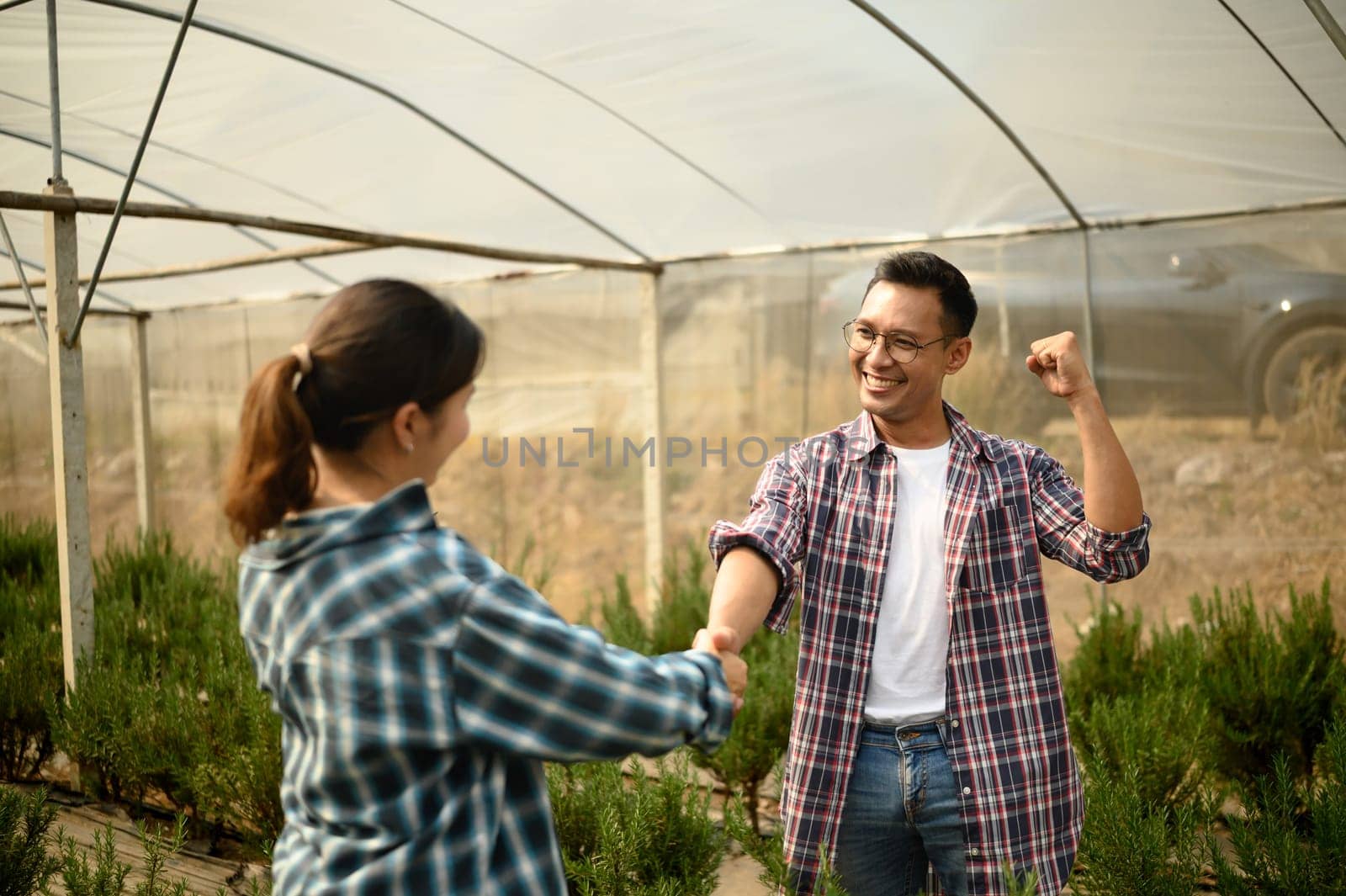 Happy farmers celebrating a successful business deal with handshake inside a greenhouse.