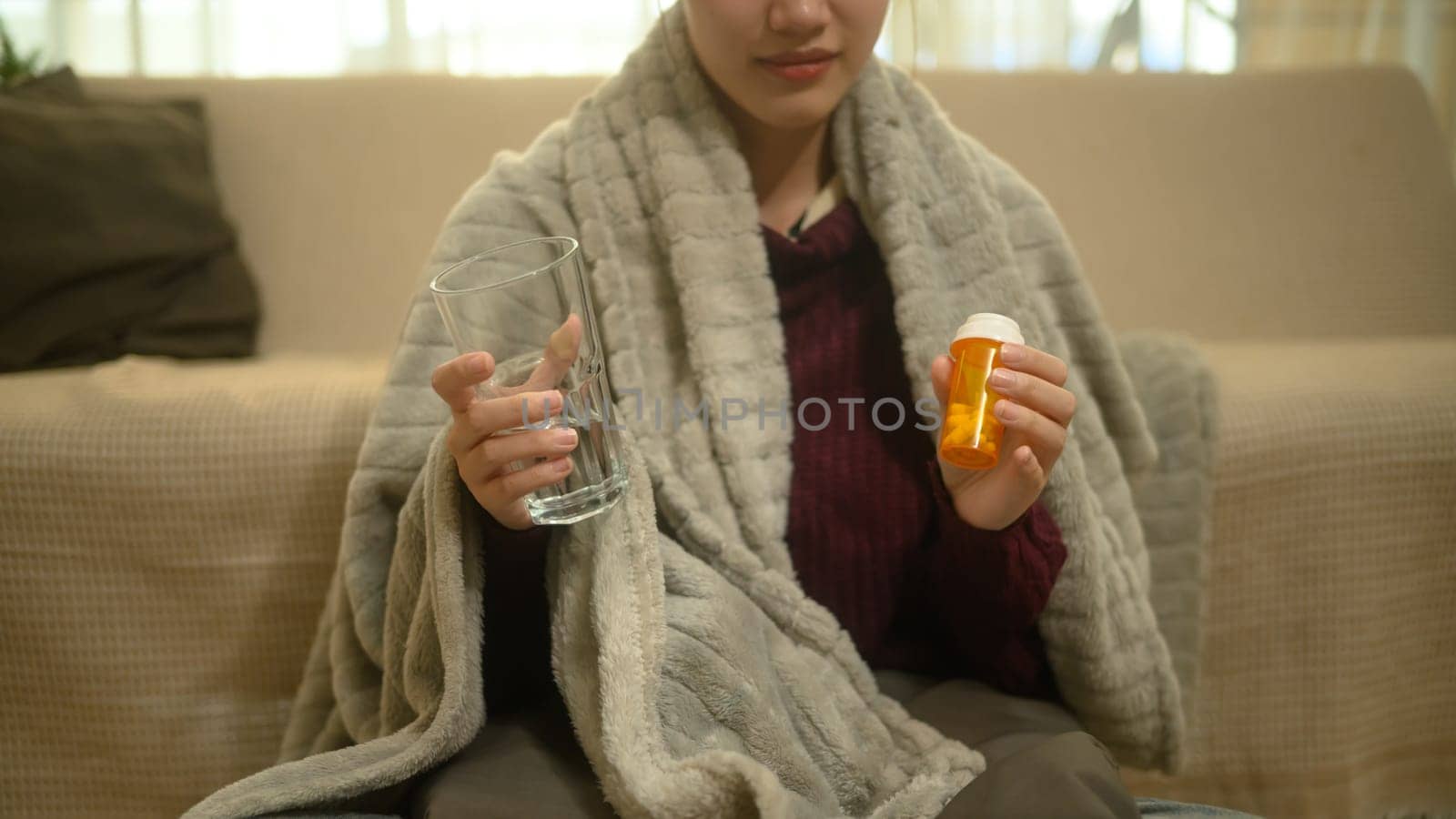 Sick young woman wrapped in a warm blanket and taking medicine for recovery.