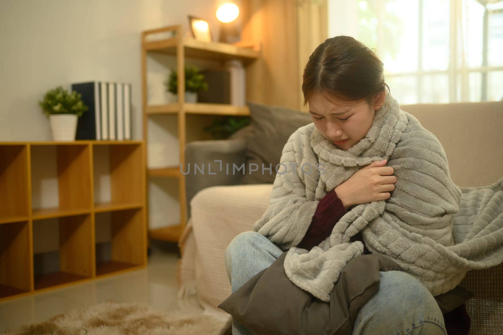 Sick woman wrapped in blanket, suffering from fever or flu.