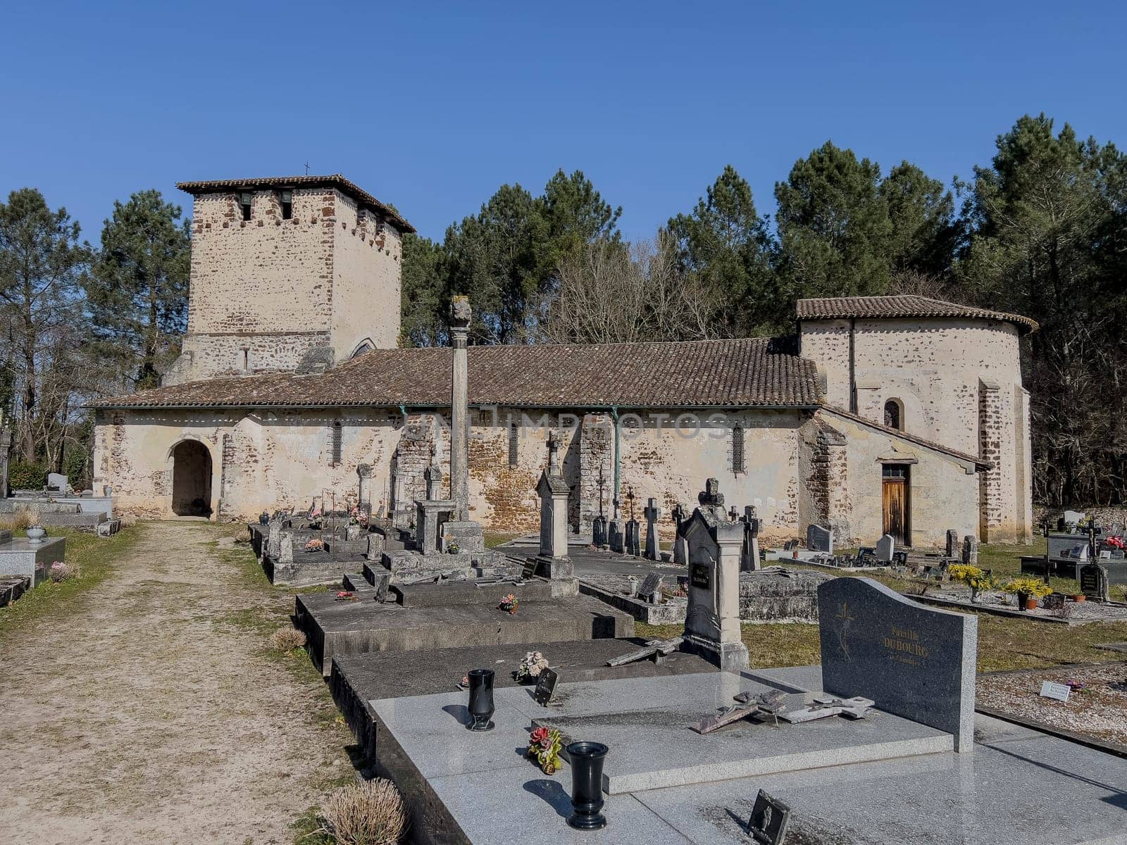Eglise Saint Pierre stands in Mons, Gironde, France, featuring distinct medieval architecture surrounded by a serene cemetery under a clear blue sky, inviting reflection and exploration.