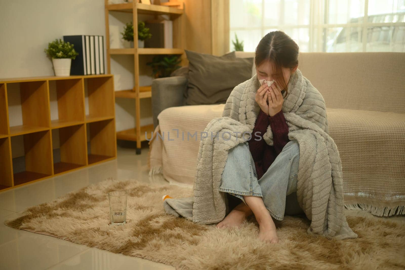 Young woman suffering from a cold or flu, sneezing while wrapped in a blanket.