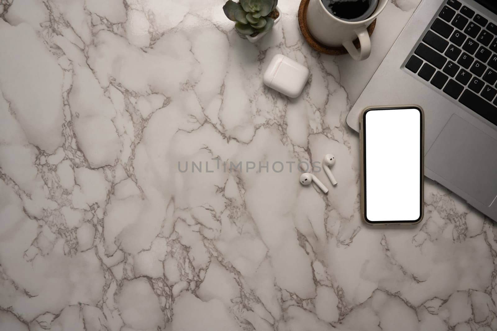 Stylish marble desk with laptop, smartphone, wireless earbuds and a coffee cup.