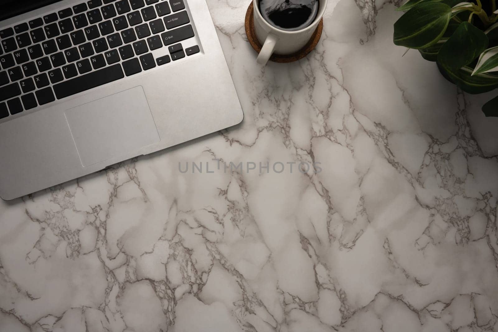 top-view of a stylish marble desk featuring a sleek laptop, a cup of black coffee, and a potted plant..