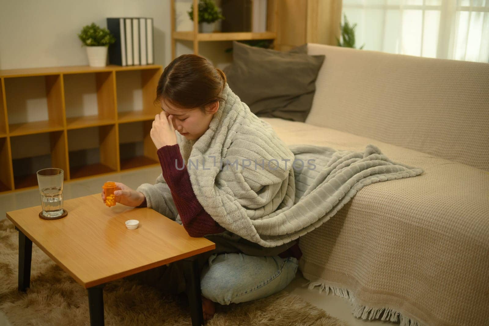 Sick young woman wrapped in a warm blanket and taking medicine for recovery.