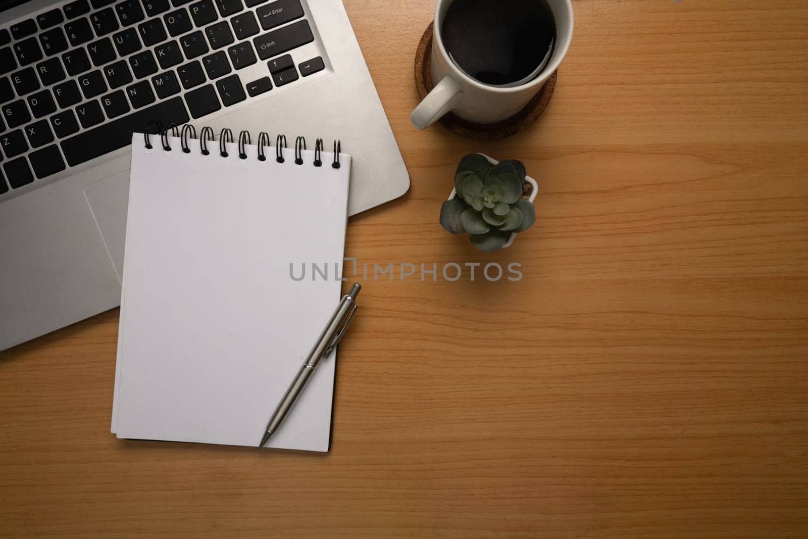Minimalist workspace with laptop, blank notebook, a cup of black coffee, and small succulent plant.