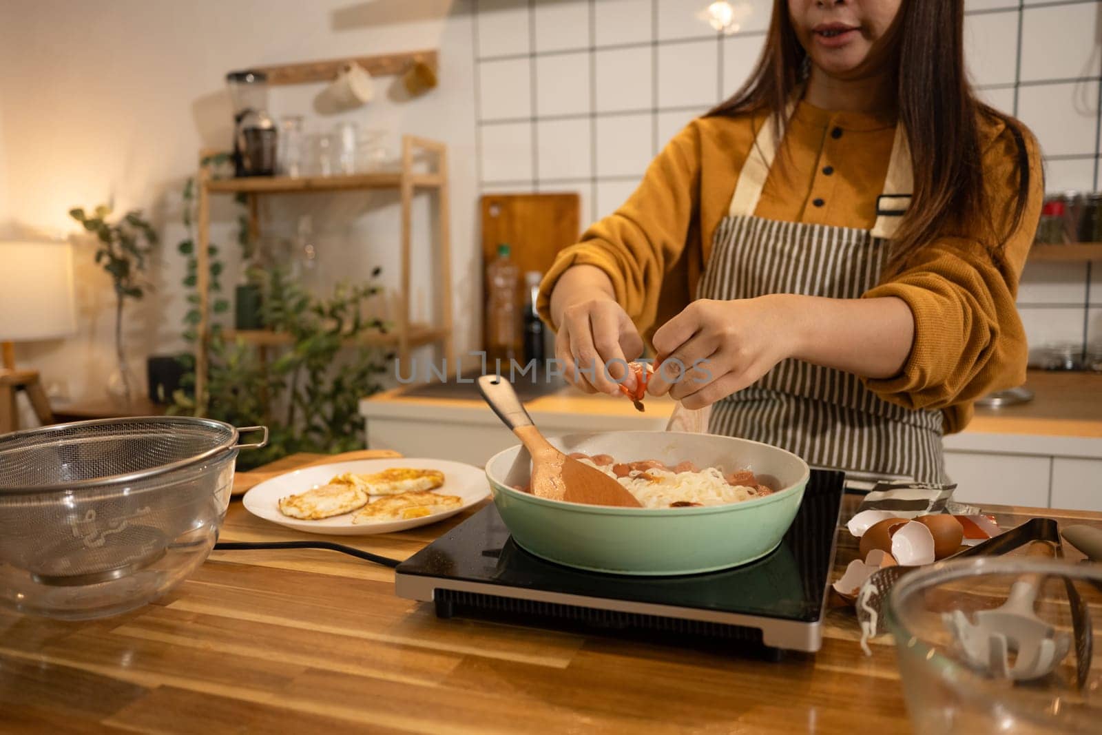 Cropped shot woman adding fresh ingredients to a pan of noodles.