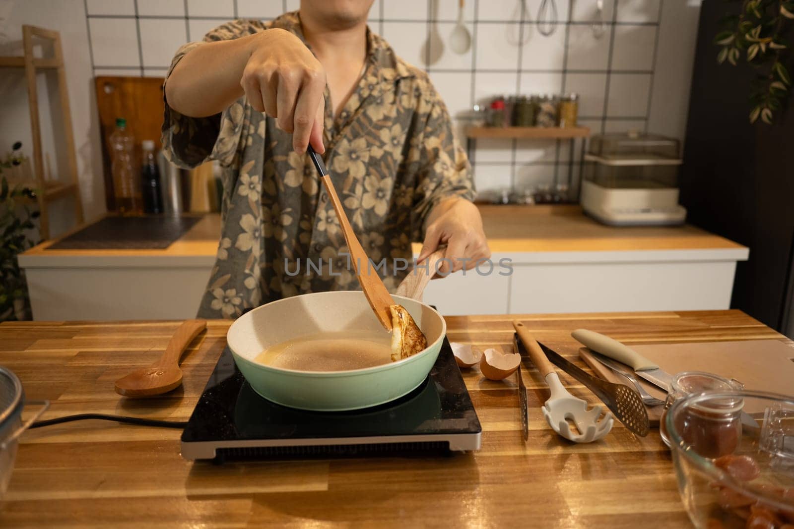 Close up of hands flipping a fried egg in ceramic pan, preparing breakfast in a home kitchen.