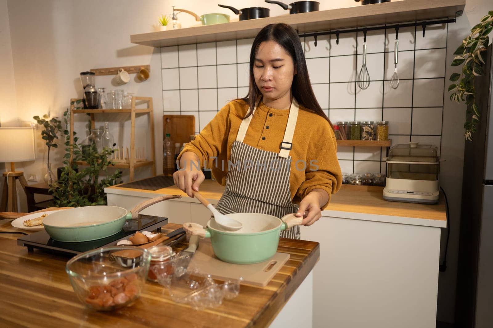Young Asian woman wearing apron preparing meal in a warm kitchen.