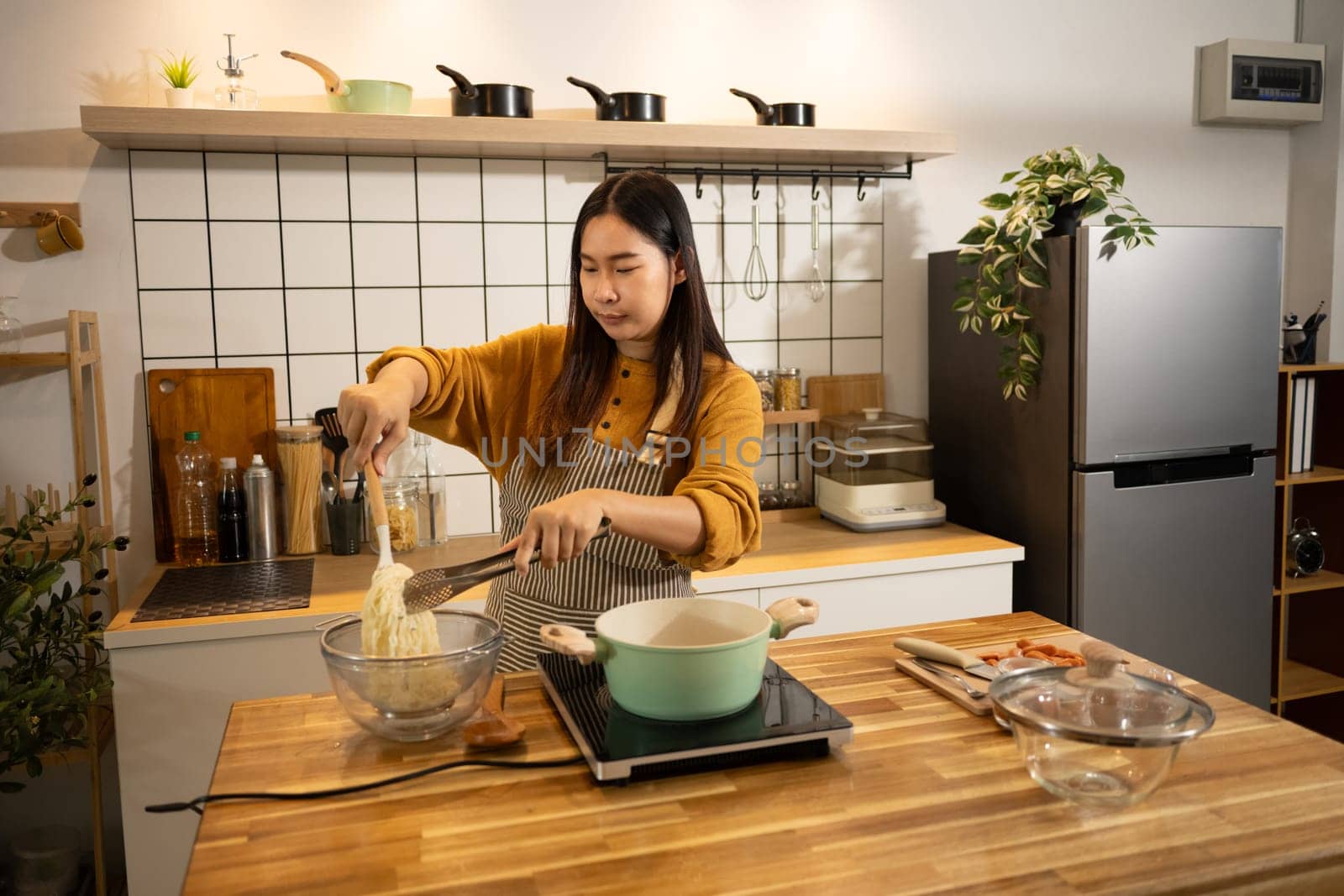 Young asian woman in an apron cooking a simple meal in her home kitchen.