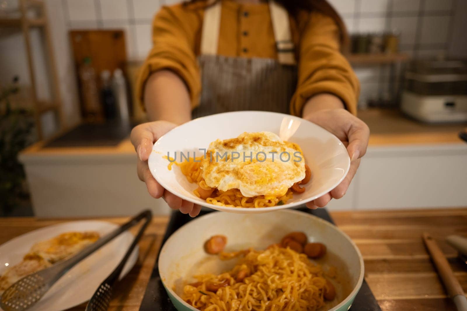 Close up of woman holding a plate of spicy noodles topped with a fried egg.