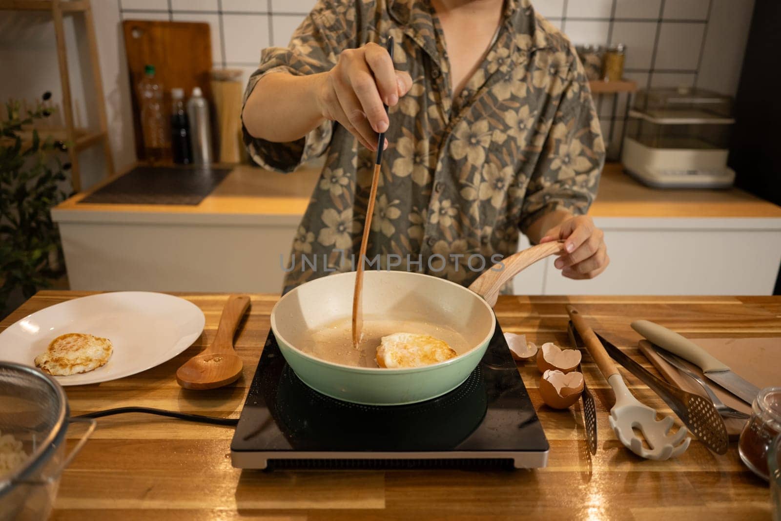 Young man preparing breakfast, frying eggs in a ceramic pan.