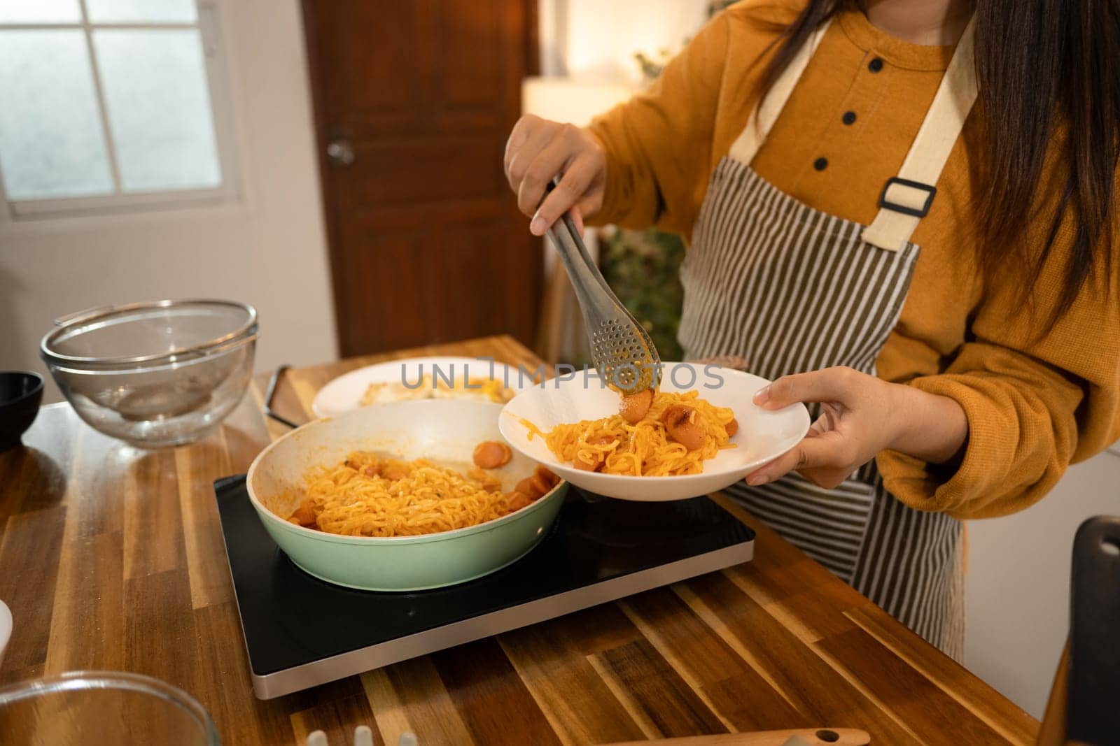 Close up of woman serving a plate of flavorful noodles with sausages.