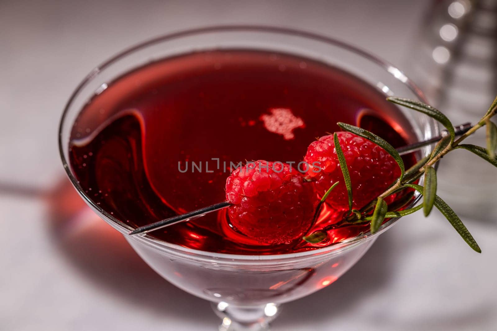 Refreshing red cocktail garnished with fresh raspberries and a sprig of rosemary, served in an elegant martini glass
