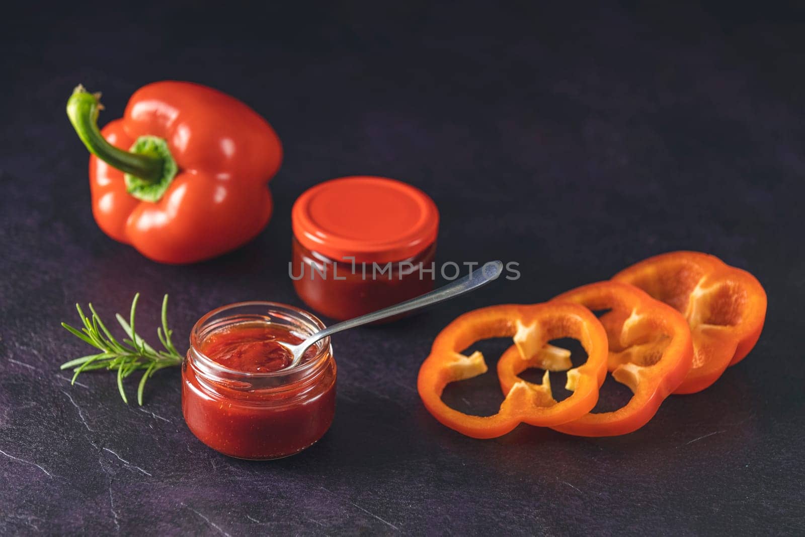 Jars of delicious homemade sauce with fresh red bell peppers and rosemary, creating a vibrant culinary scene