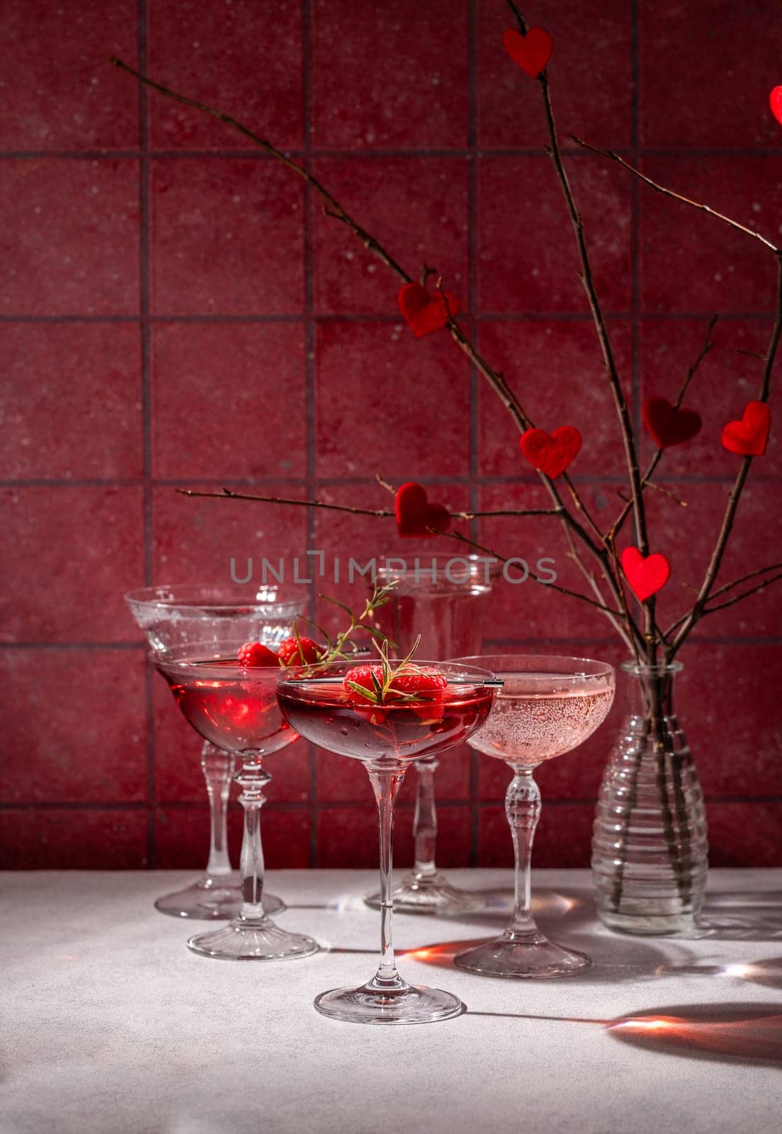 Elegant valentine's day cocktails garnished with raspberries and rosemary, creating a romantic atmosphere against a red backdrop