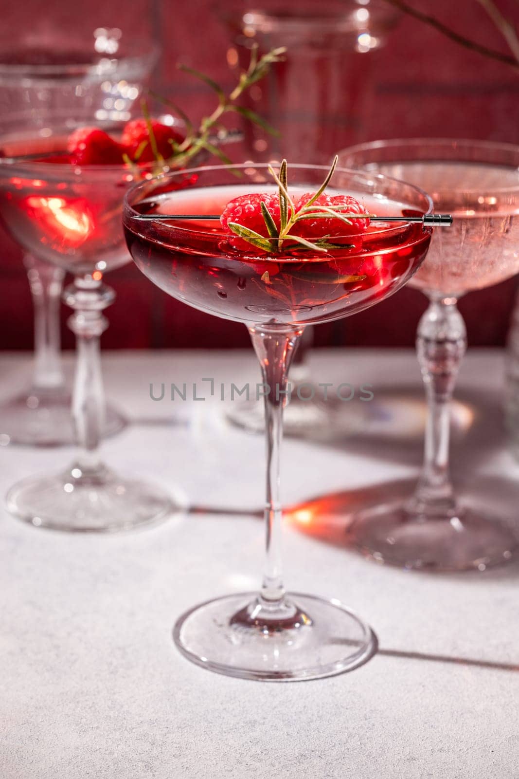 Coupe glasses filled with vibrant red cocktails, adorned with fresh raspberries and a fragrant rosemary sprig, create a sophisticated and festive atmosphere