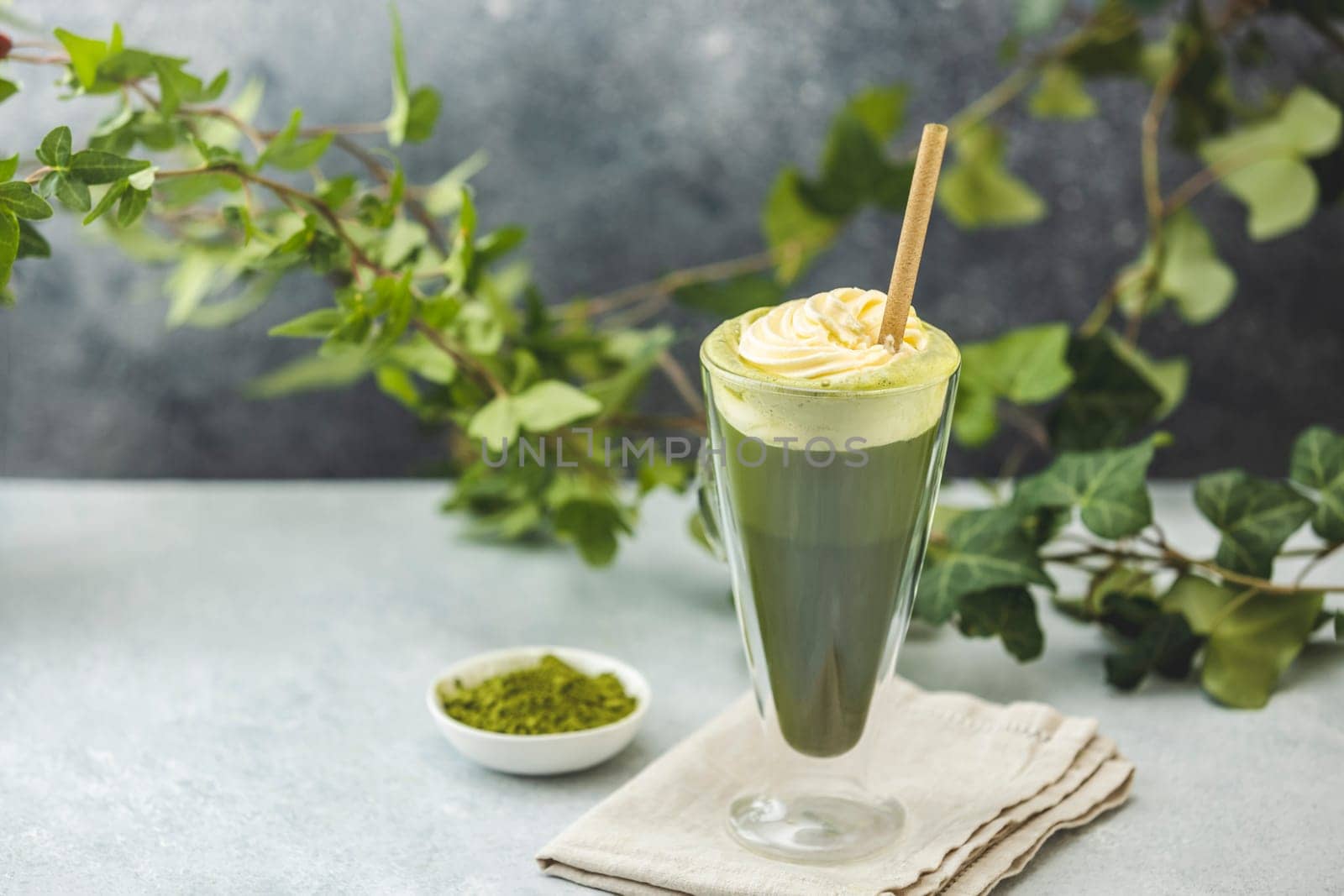 Preparing an iced matcha latte topped with whipped cream and garnished with fresh ivy branches, creating a refreshing summer drink