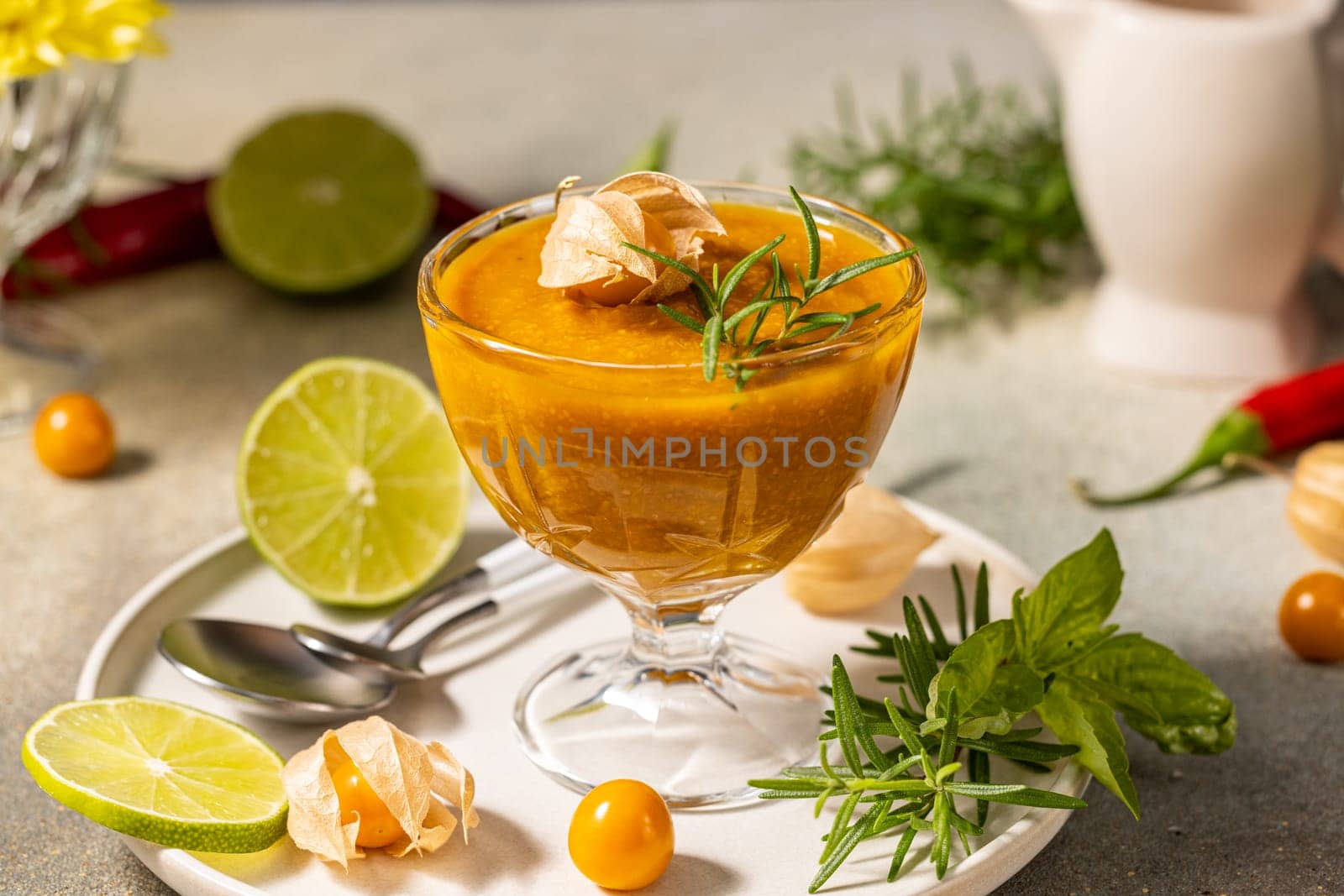 Aguaymanto cream served in a glass cup, decorated with a physalis and rosemary, accompanied by lime slices, all on a white plate