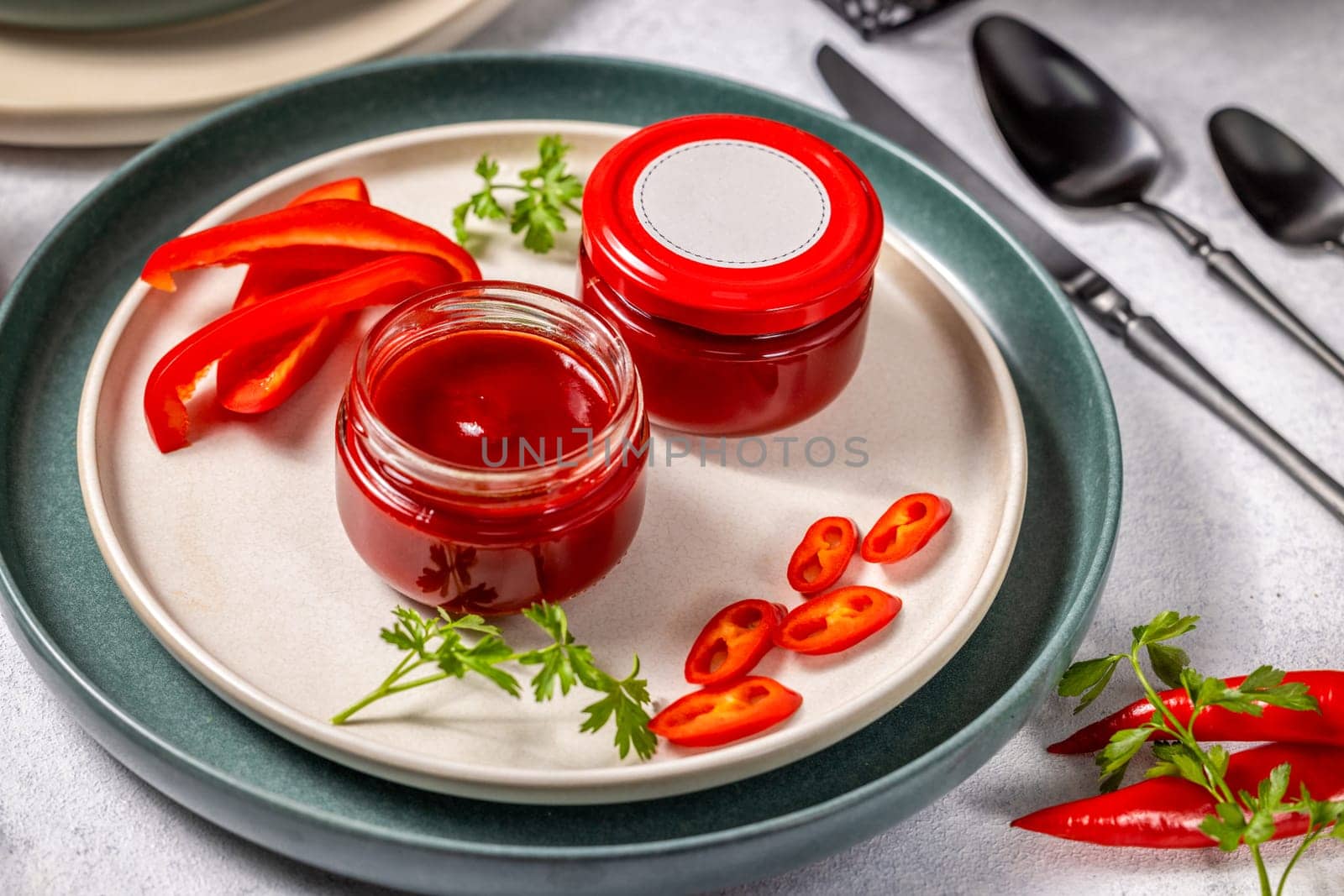 Two jars of homemade red pepper sauce are presented on an elegant plate, garnished with fresh chili pepper slices and herbs, ready to enhance any meal