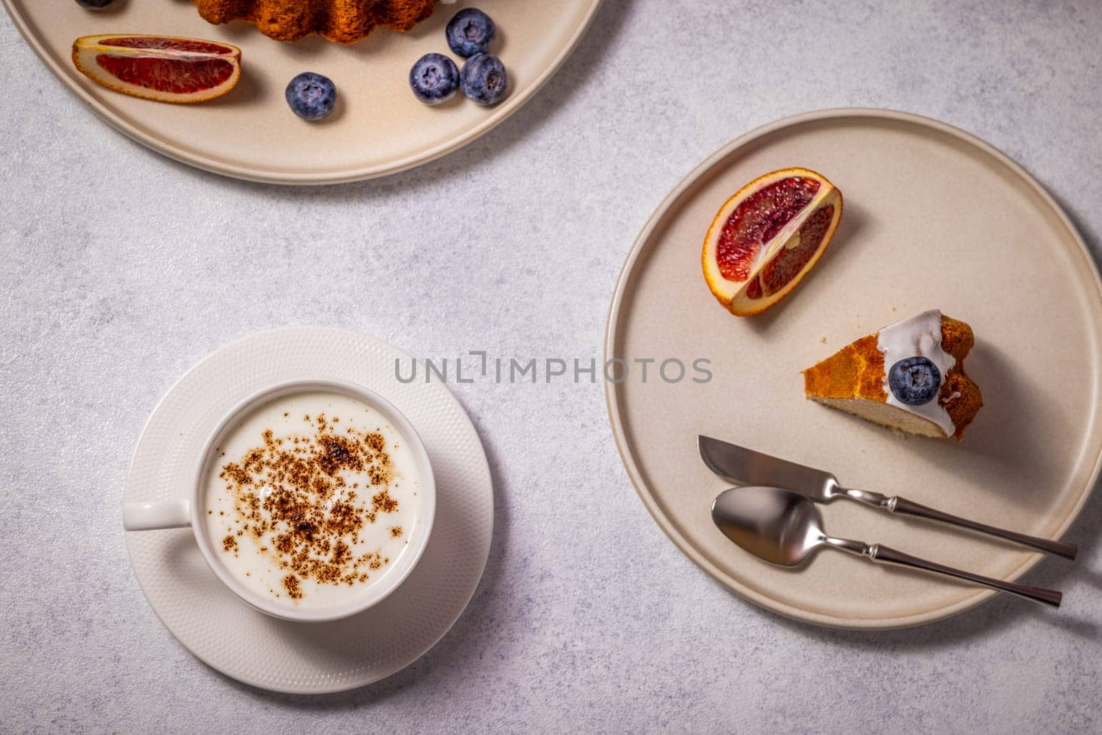 Enjoying a slice of delicious cake with a cup of cappuccino, fresh orange slices, and blueberries, creating a delightful breakfast or snack