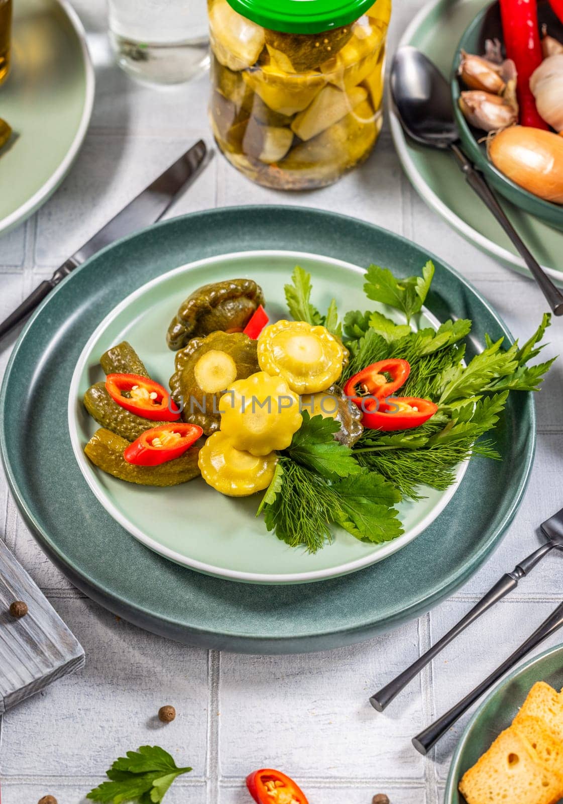 Pickled pattypan squash, cucumbers, and chili peppers served on a plate with fresh herbs, creating a vibrant and appetizing dish