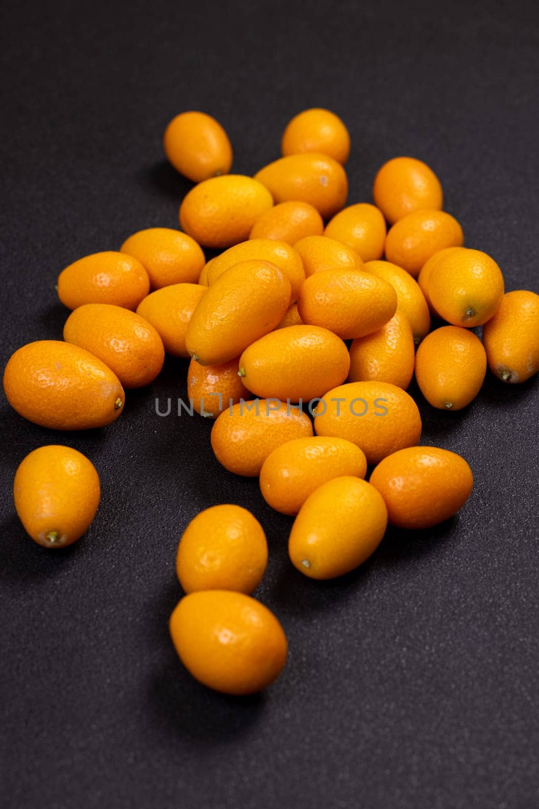 Fresh kumquats scattered across a dark surface, showcasing a vibrant contrast of colors and textures, highlighting their juicy, sweet, and sour appeal