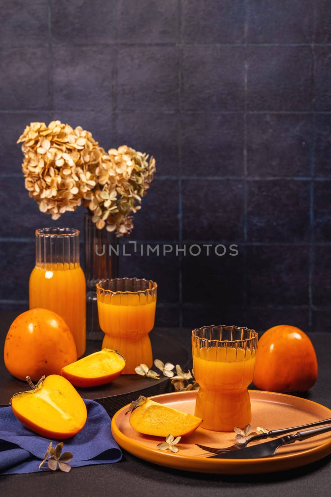 Persimmon juice served in elegant glasses with fresh and ripe persimmon fruits, accompanied by dried flowers, creating a cozy autumn atmosphere
