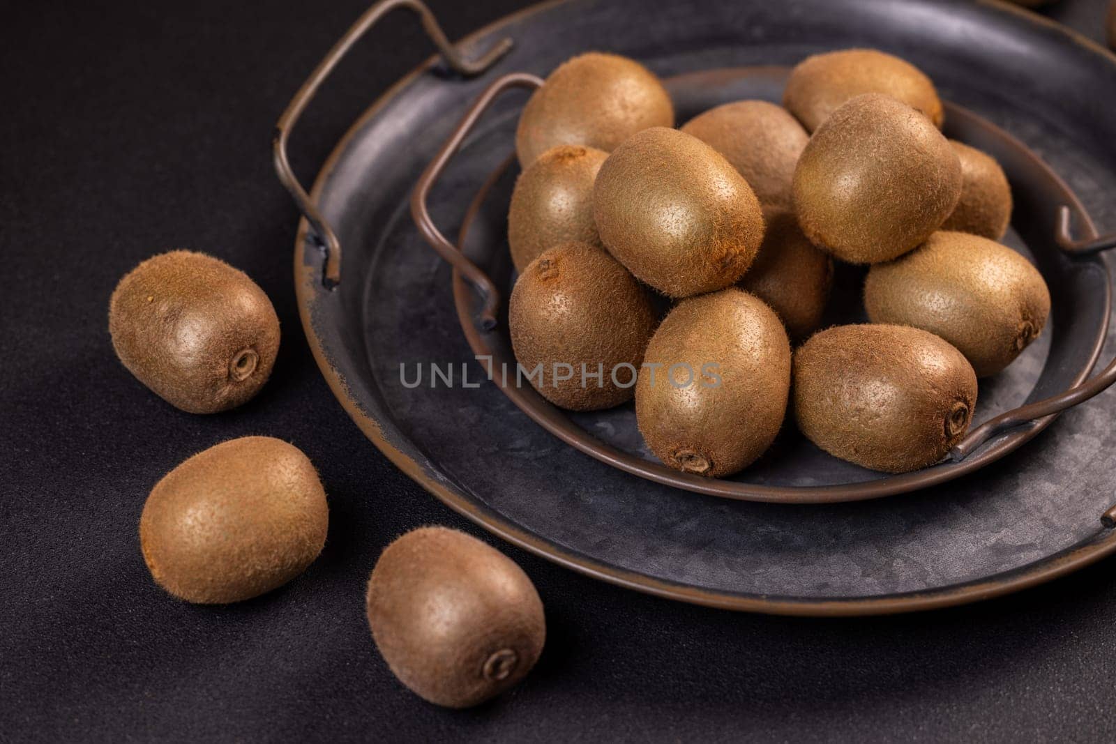Ripe kiwi fruits are neatly arranged on a dark metal tray, creating a visually appealing display against a black background