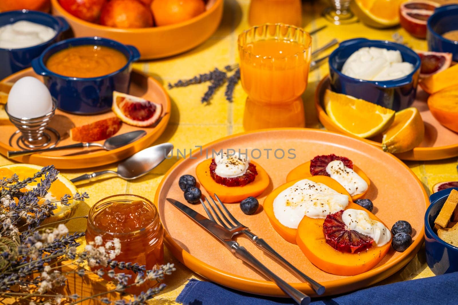 Vibrant breakfast scene featuring persimmon slices with ricotta, blood orange, and honey, alongside fresh fruit and yogurt