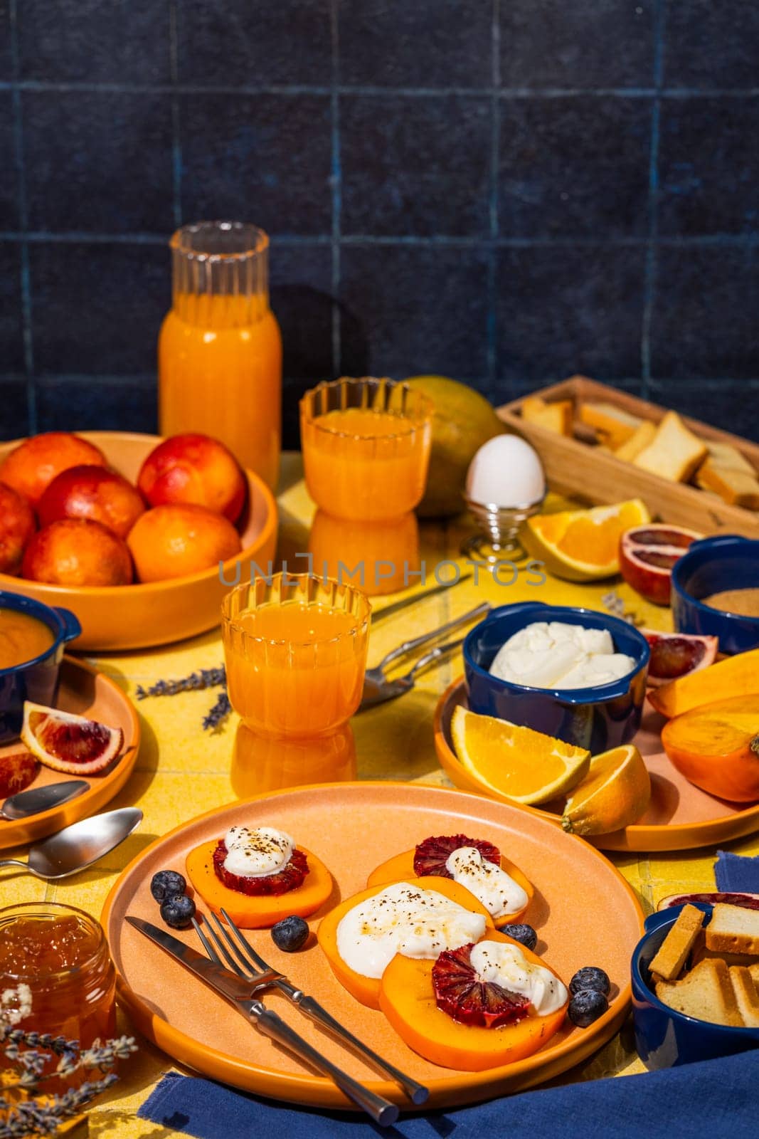 Slices of persimmon topped with ricotta, blood orange, and blueberries, served with orange juice and fresh fruit for a healthy breakfast
