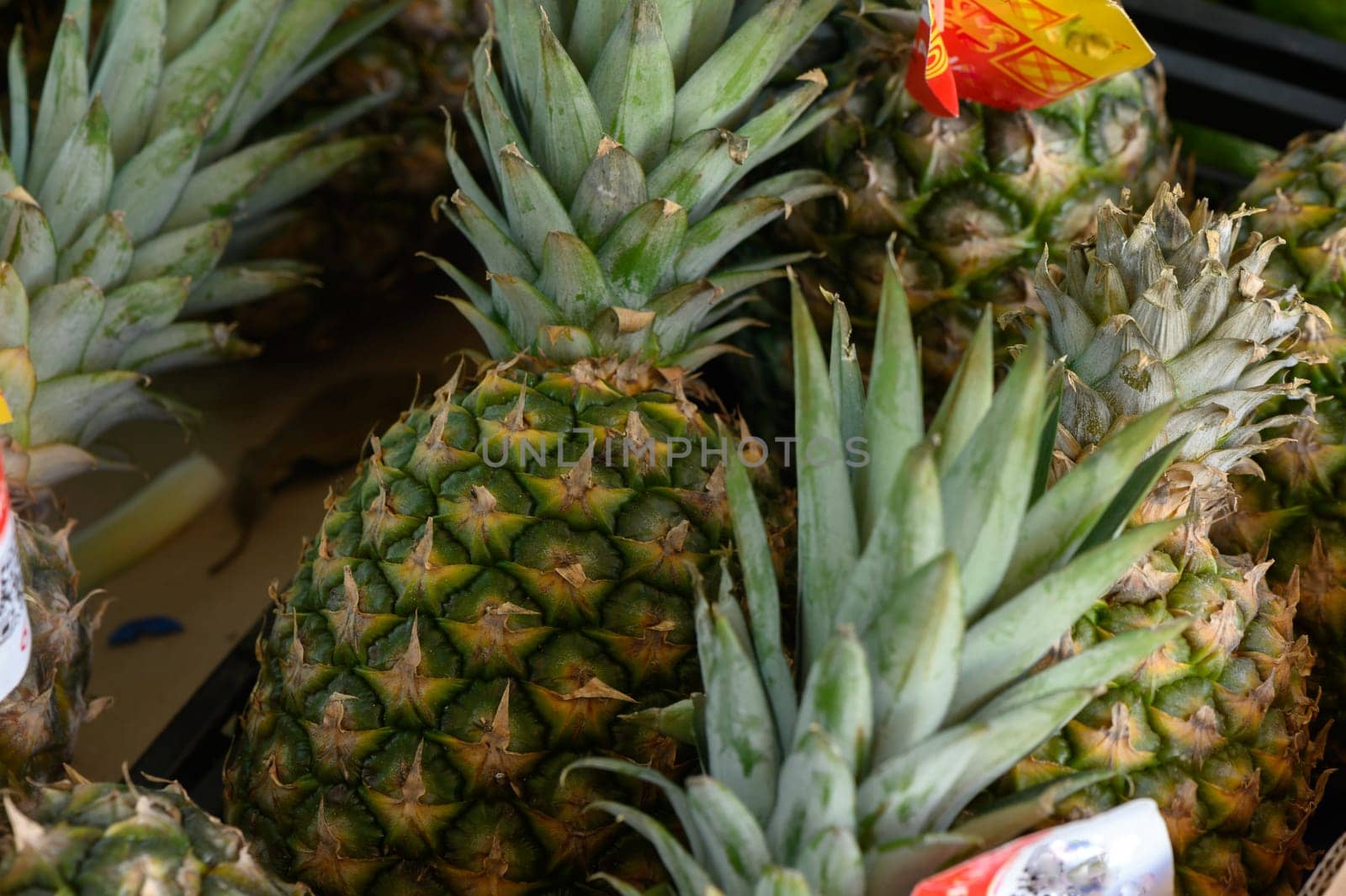 Colorful pineapples stand stacked in a bustling market, their green crowns reaching for the sky. The warm light highlights their textured skins as shoppers browse nearby.