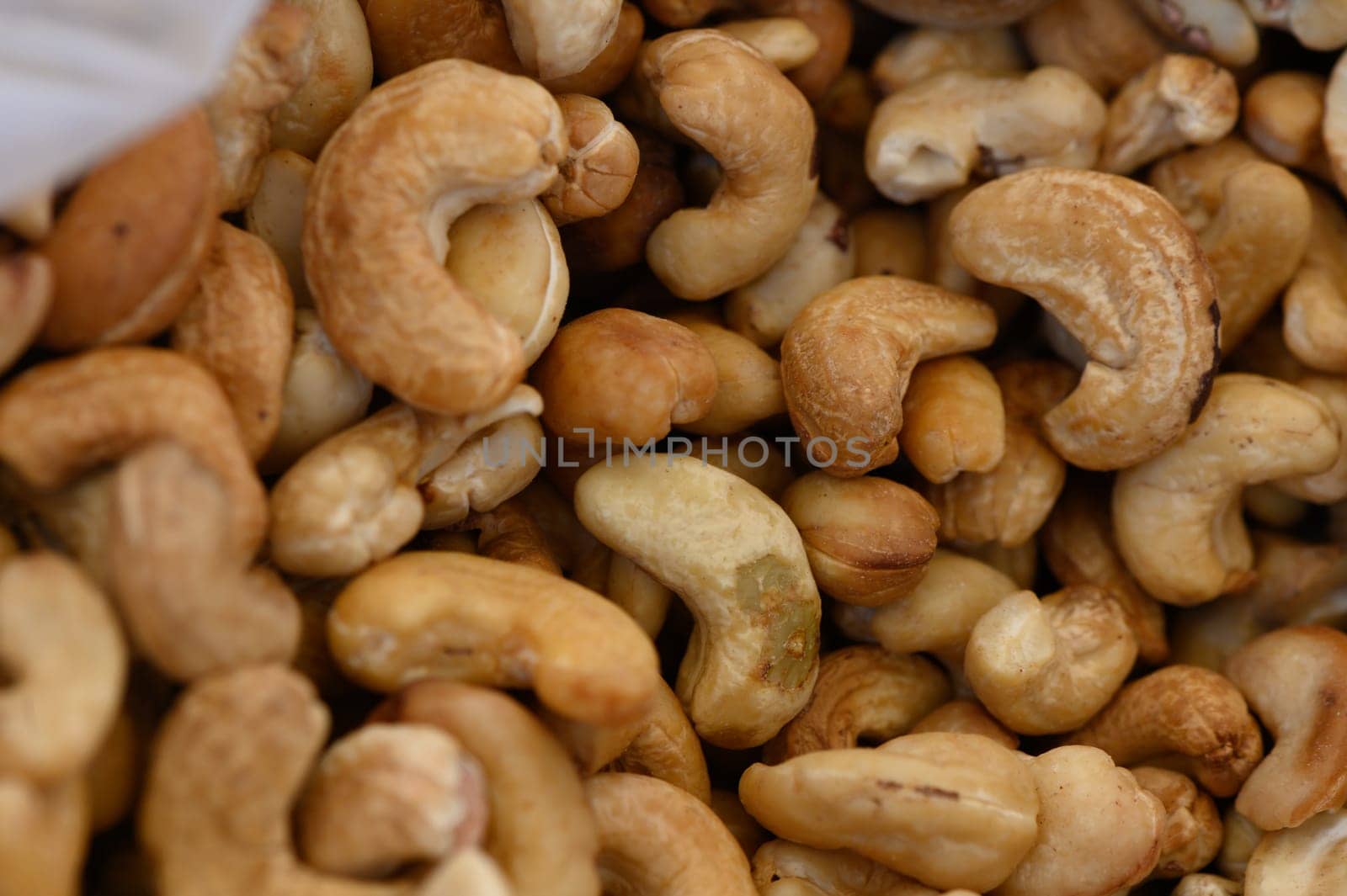 In a vibrant marketplace, cashew nuts are displayed in abundance, highlighting their varied shapes and textures. The sunlight enhances their earthy tones, creating a rich visual feast.