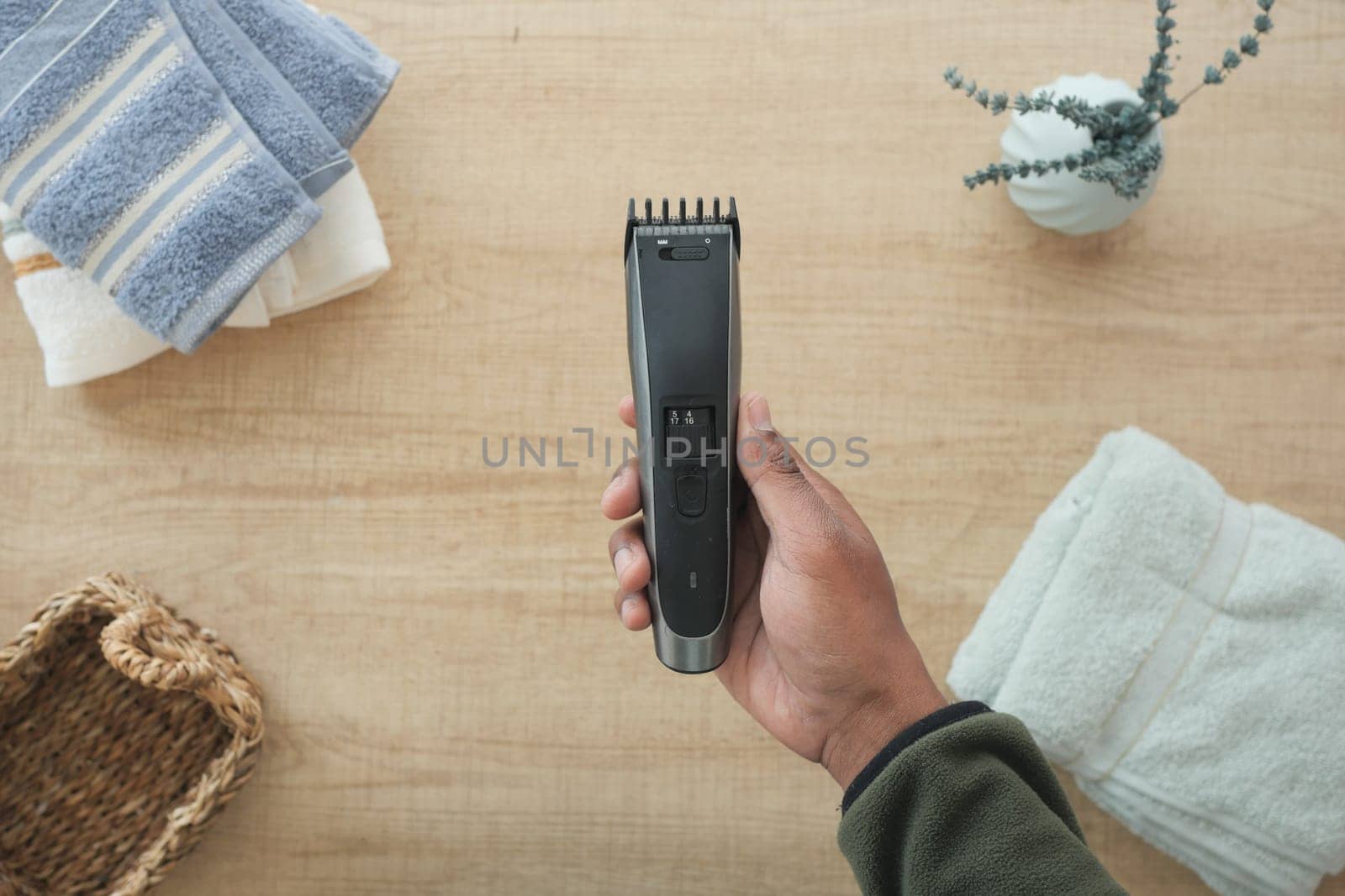 A person uses a hair clipper amidst clean towels and decor in the bathroom.