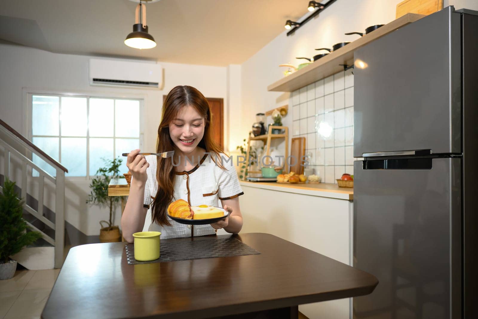 Beautiful young woman enjoying a delicious breakfast in a cozy home kitchen.