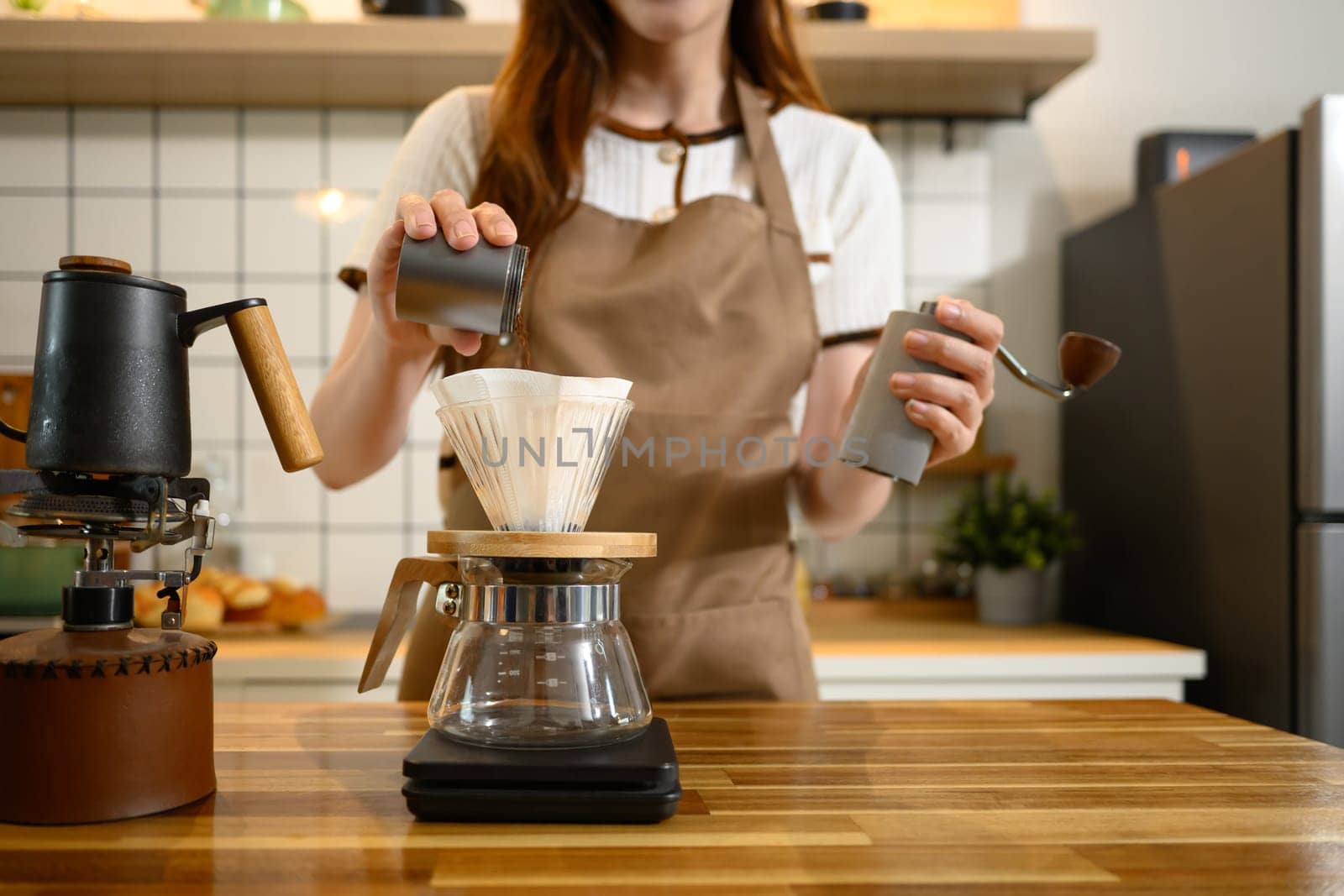 Close up of hand pouring ground coffee into a paper filter in a glass dripper over a scale.