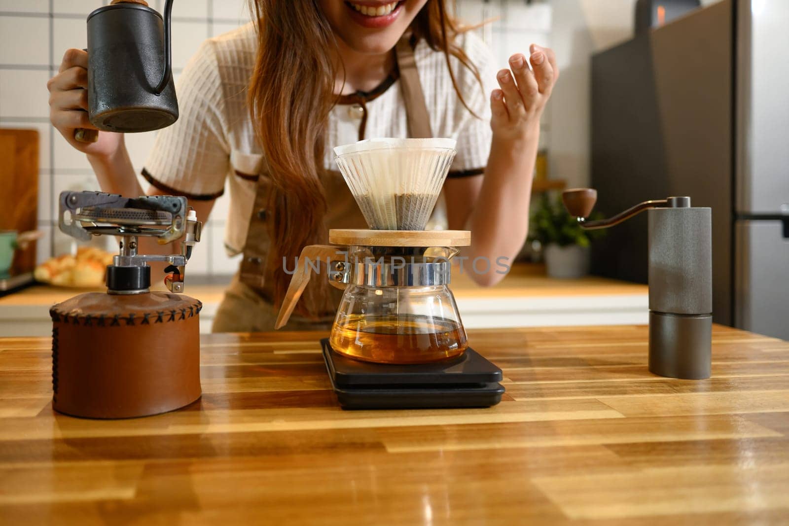 Happy young woman wearing apron preparing a fresh pour over coffee in stylish kitchen.