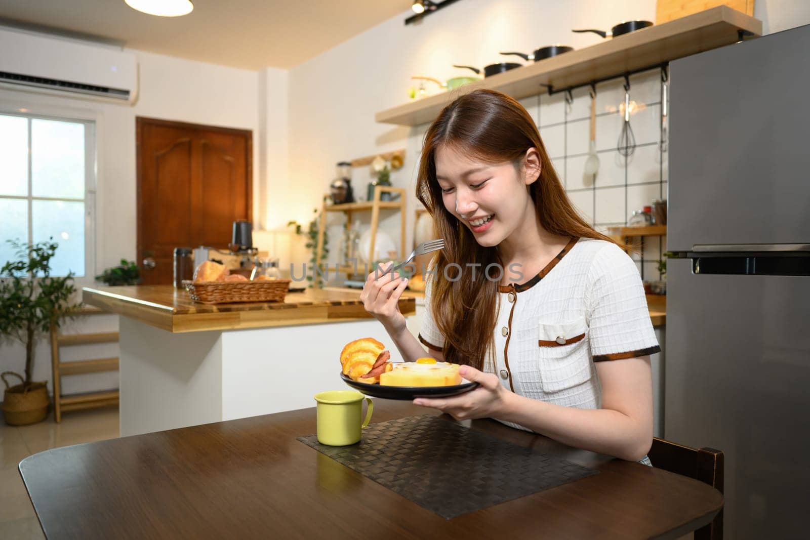 Happy young woman enjoying a delicious breakfast in a cozy home kitchen.